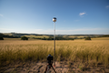 GNSS receiver mounted on surveyor's rod in open field with blue sky