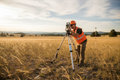 Digital total station on tripod in field with surveyor looking through eyepiece