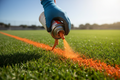 Gloved hand spraying orange marking paint on grass