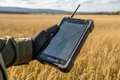Surveyor holding rugged GPS tablet with topographic map on screen in open field