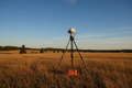 GNSS RTK base station on tripod in open field with blue sky